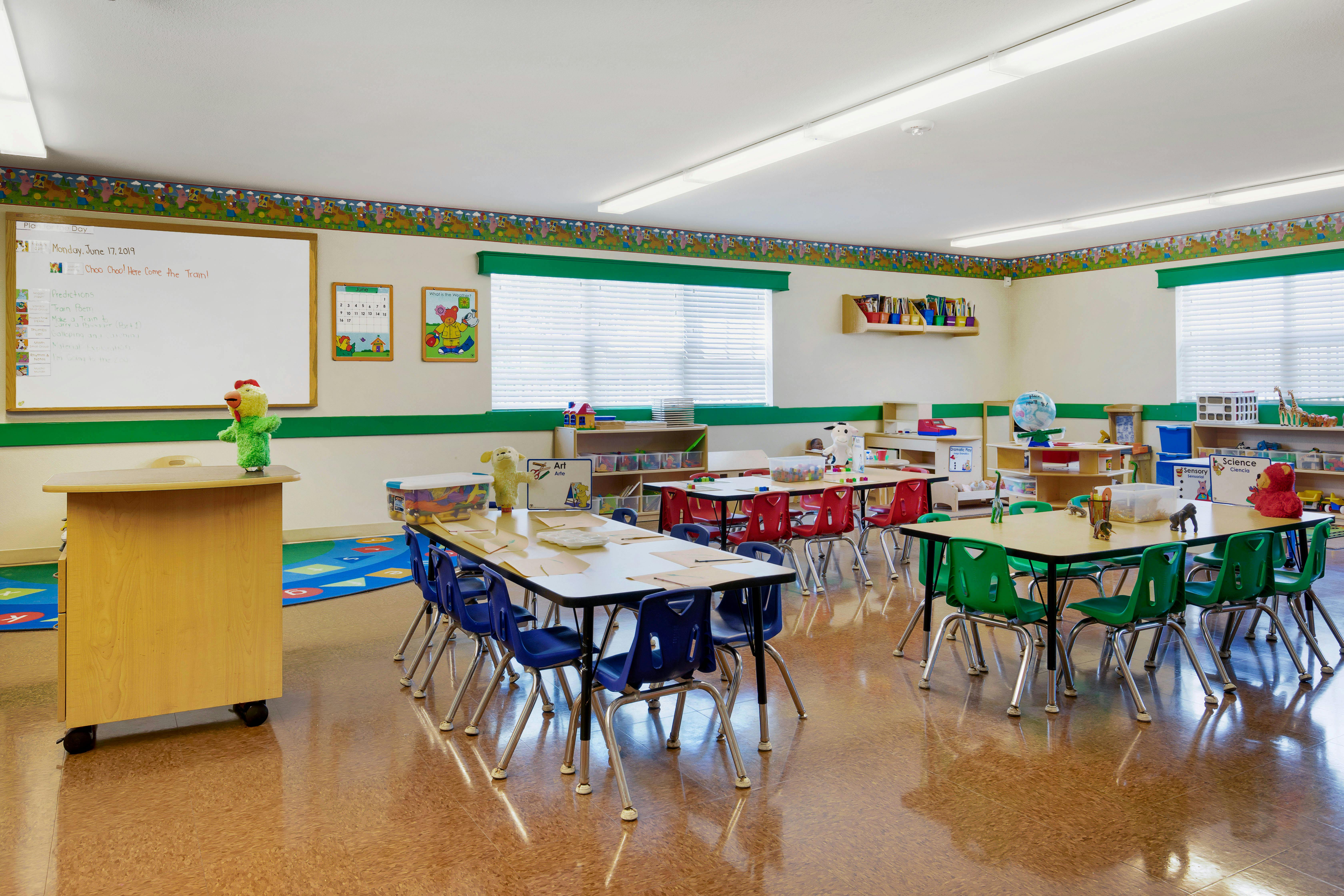 Empty classroom with small tables and chairs, whiteboard, and colorful decorations