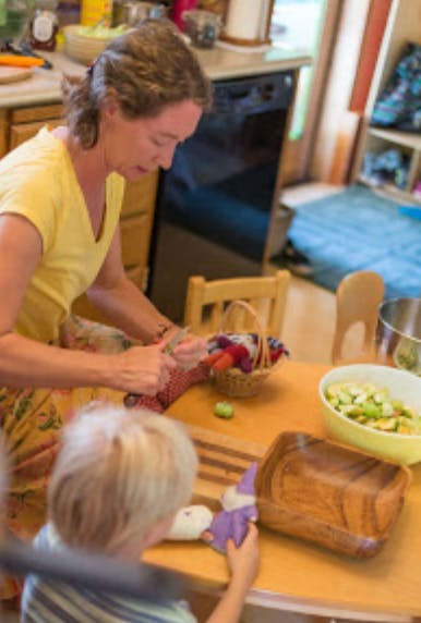 Adult and child at a table, adult cutting food, child holding a toy
