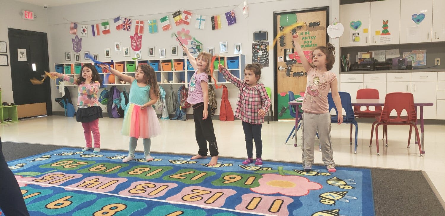 Children standing on a number rug with arms raised in a classroom