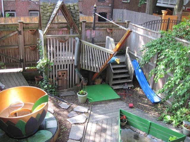 backyard play area with a playhouse, slide, stairs, and a large cup-shaped planter