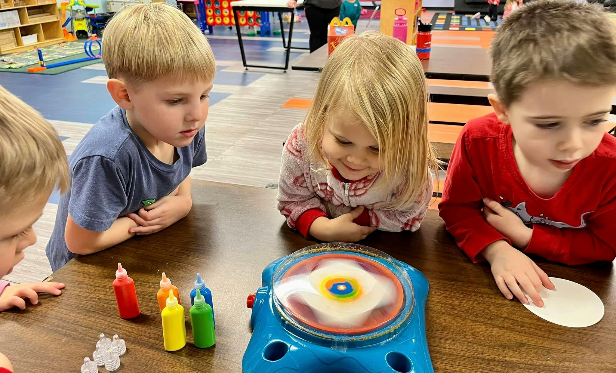 Children watching a spinning art machine on a table