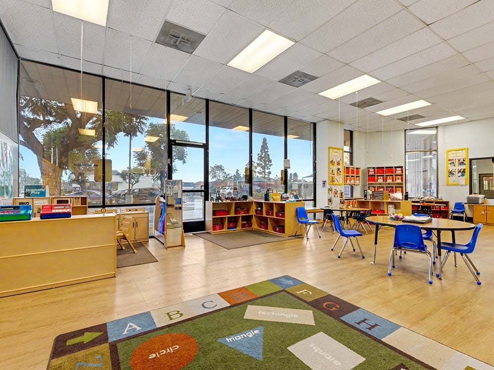 Empty classroom with small tables and chairs, and a colorful rug