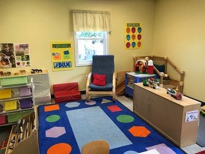 A classroom with a blue rug, shelves of toys, and a rocking chair
