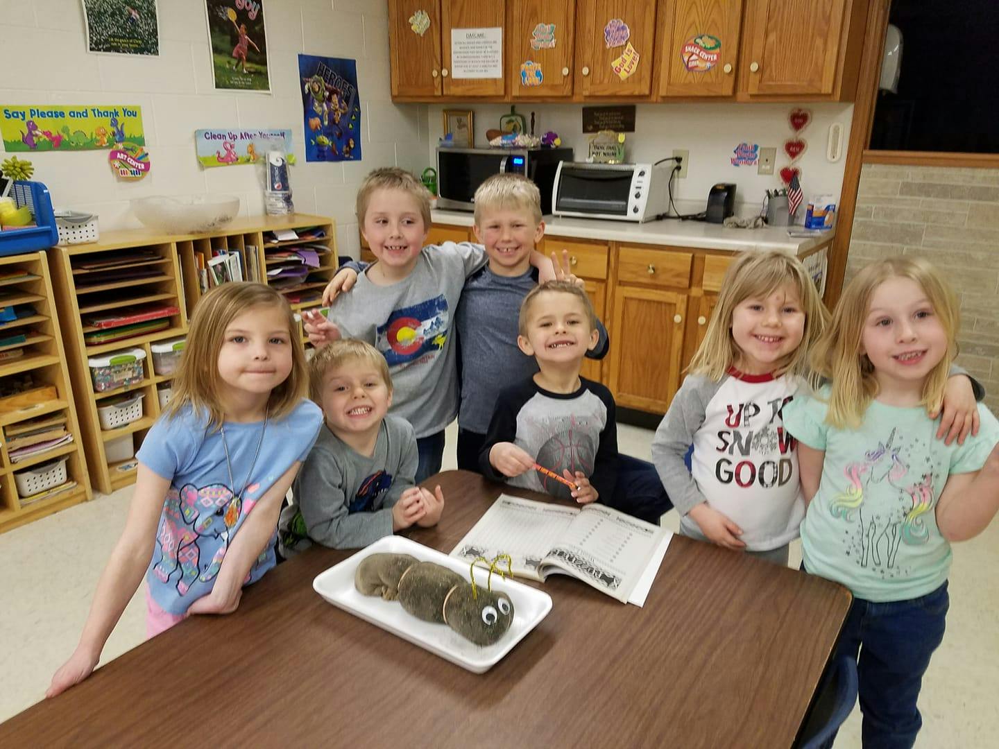 Group of children standing around a table with a caterpillar craft