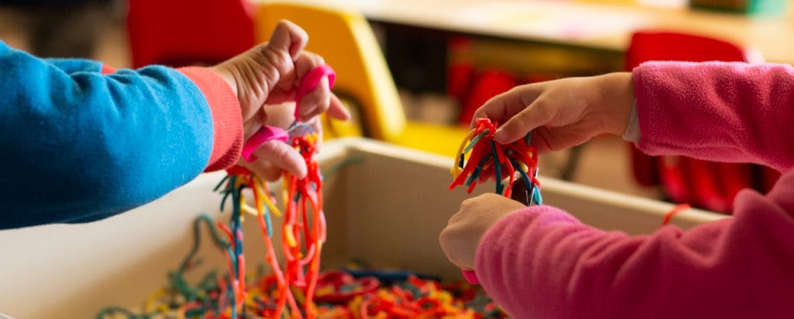 Two children's hands playing with colorful strings