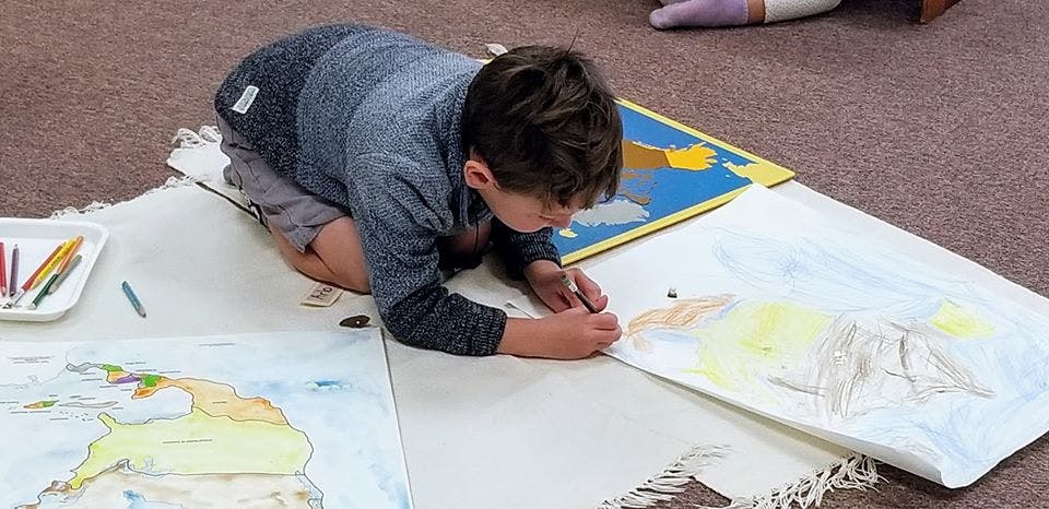 Child kneeling on floor drawing on paper