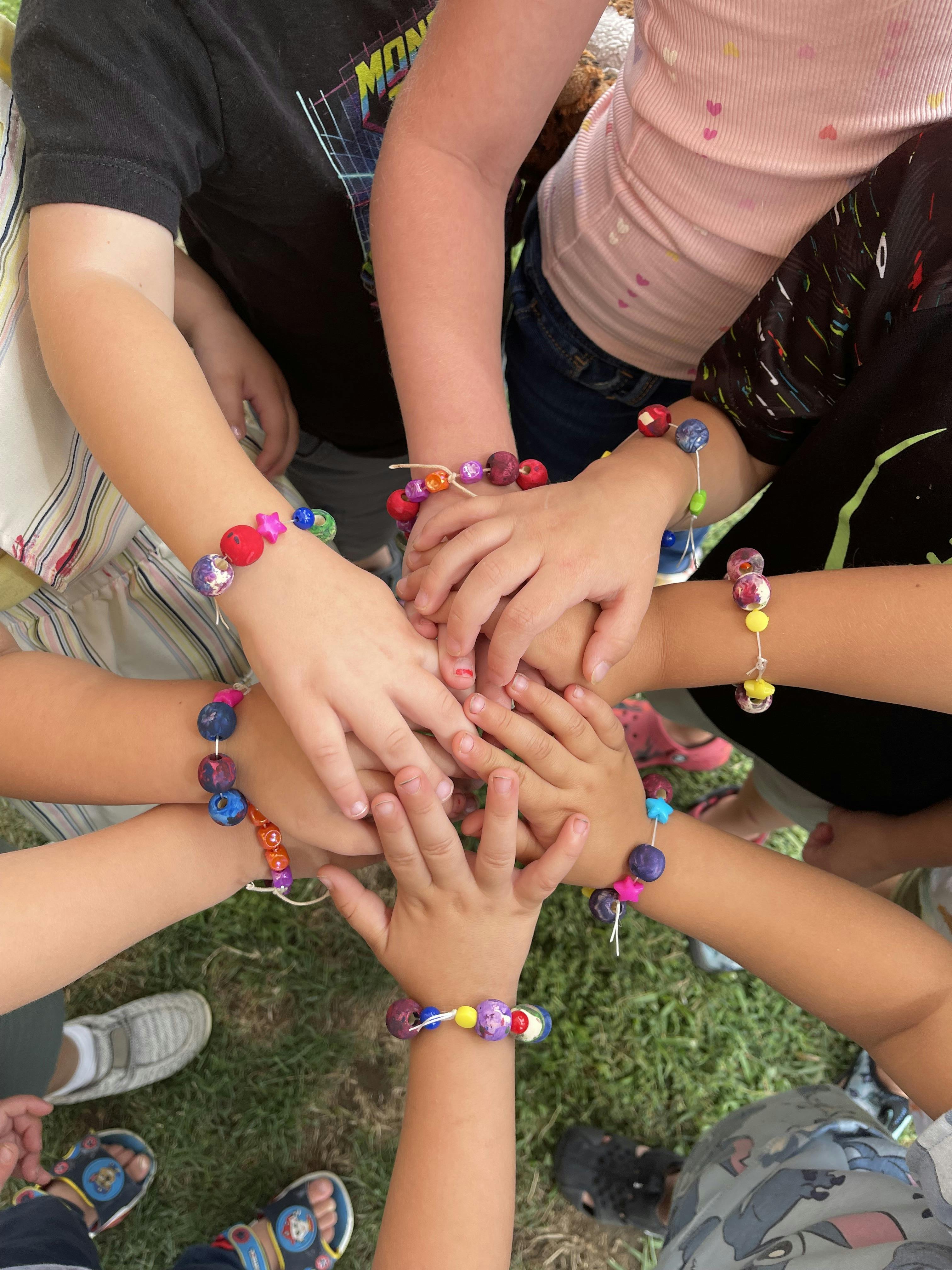 Group of children stacking hands wearing handmade bead bracelets