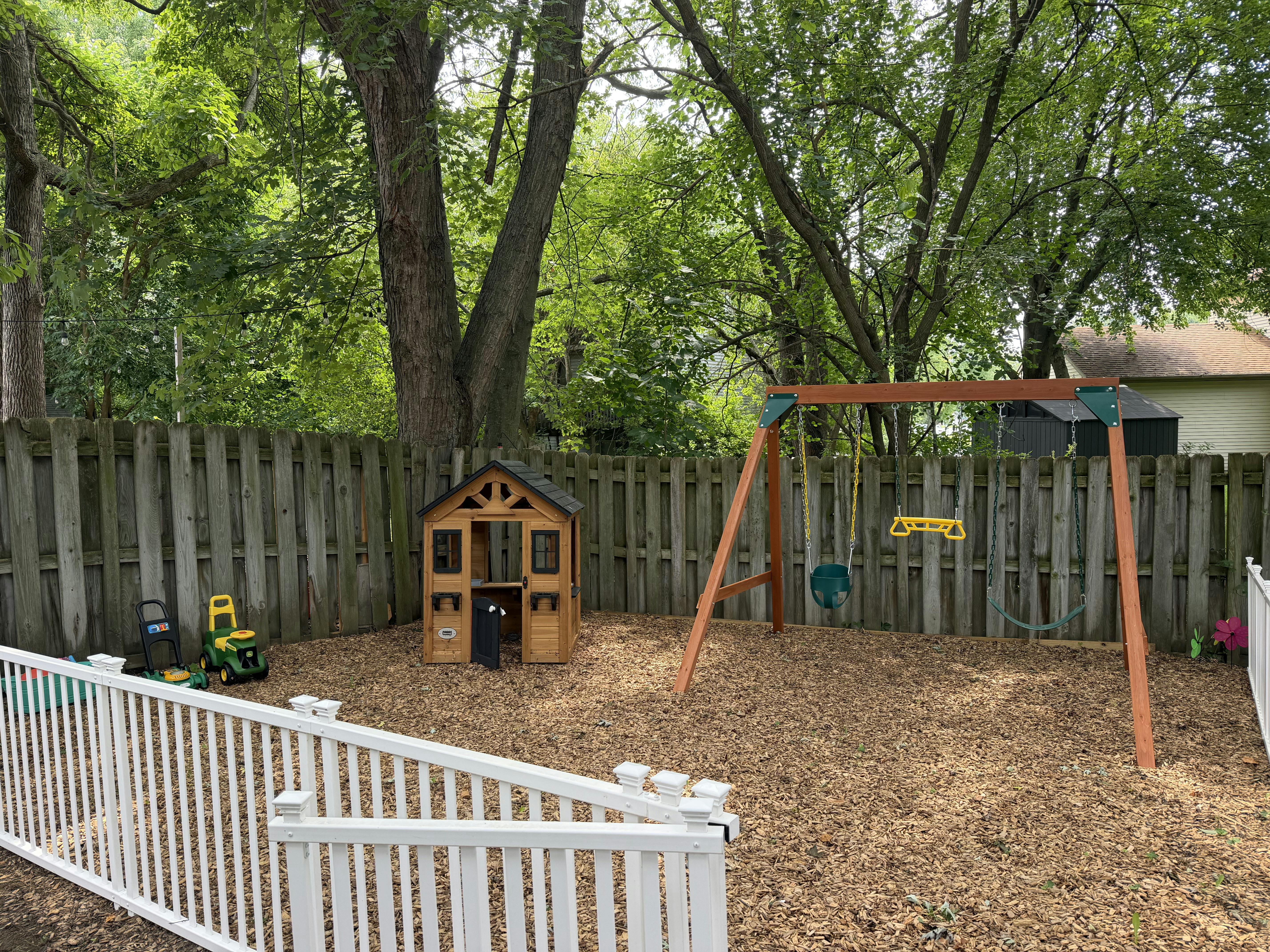 Backyard playground with a wooden playhouse and swing set on wood chips