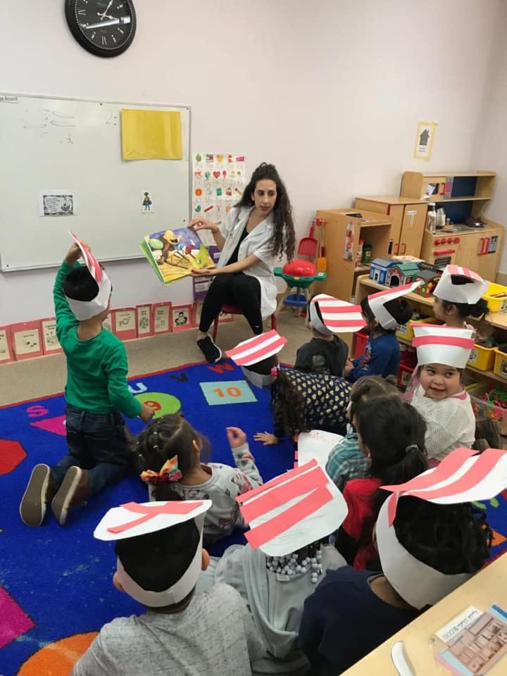 Person reading a book to children wearing paper hats in a classroom