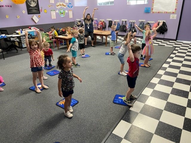 Children and an adult doing arm stretches in a classroom