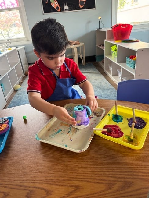Child in an apron painting a small object on a tray at a table