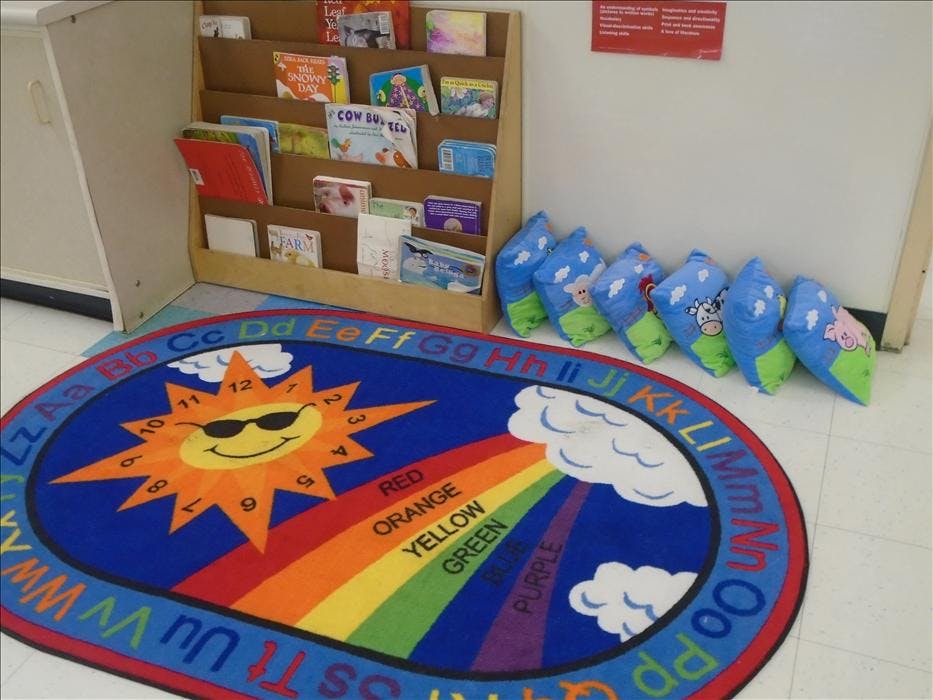 Classroom with a colorful rug featuring a sun and rainbow, and a book display
