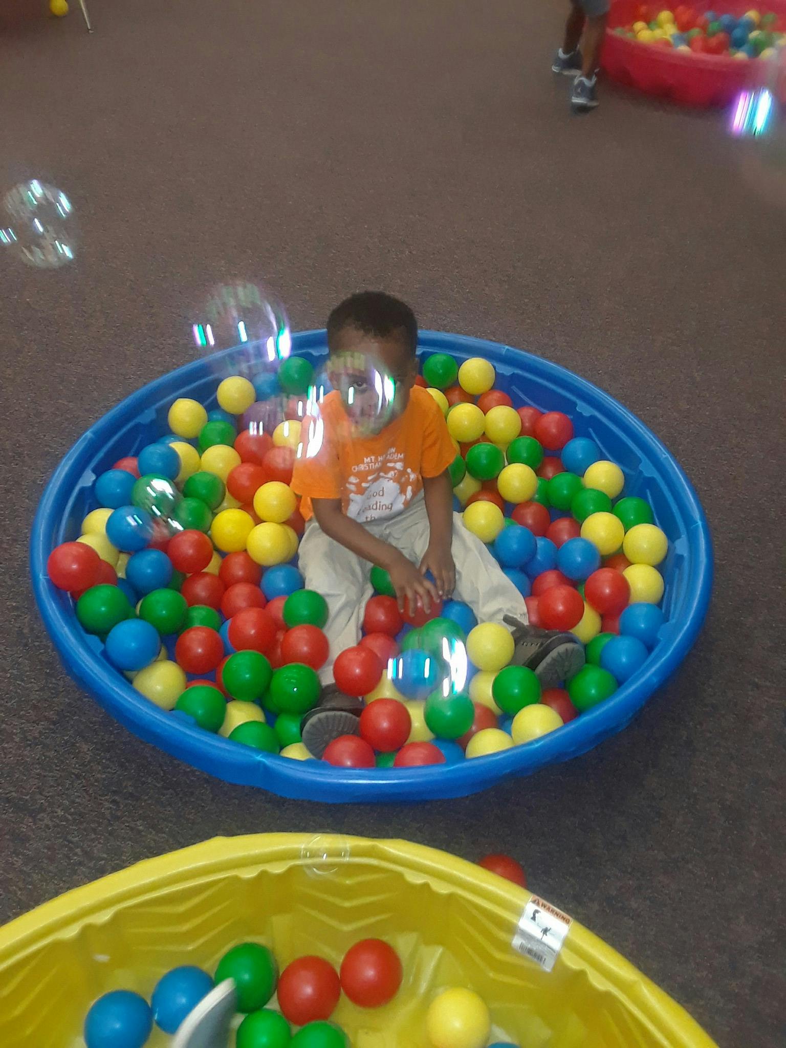 Child sitting in a blue ball pit with colorful balls and bubbles