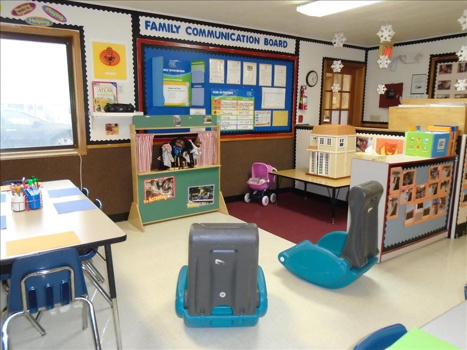 Classroom with a puppet stage, dollhouse, tables, and a family communication board