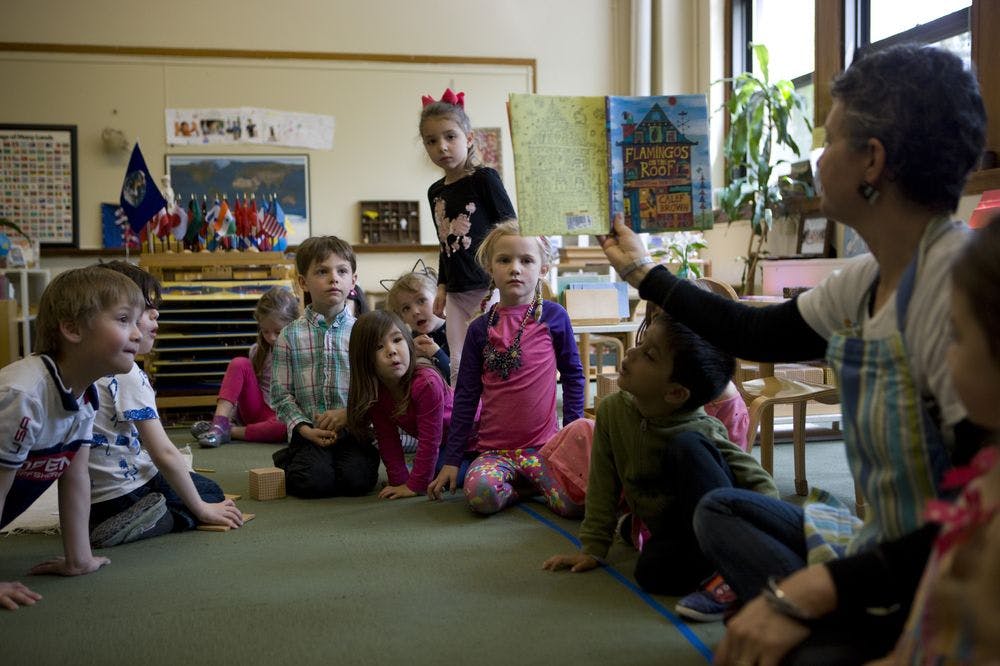 Adult reading a book to a group of children in a classroom