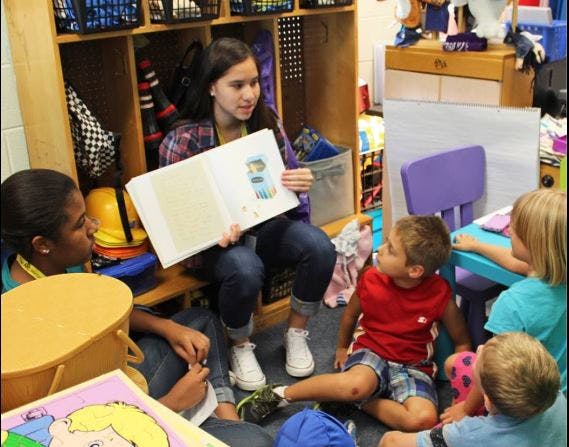 Teen reading a book to a group of children