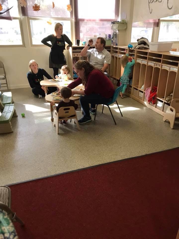 Adults and children gathered around small tables in a classroom