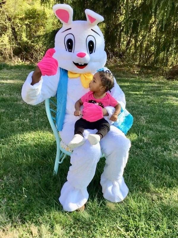 Child sitting on the lap of a person in a rabbit costume outdoors