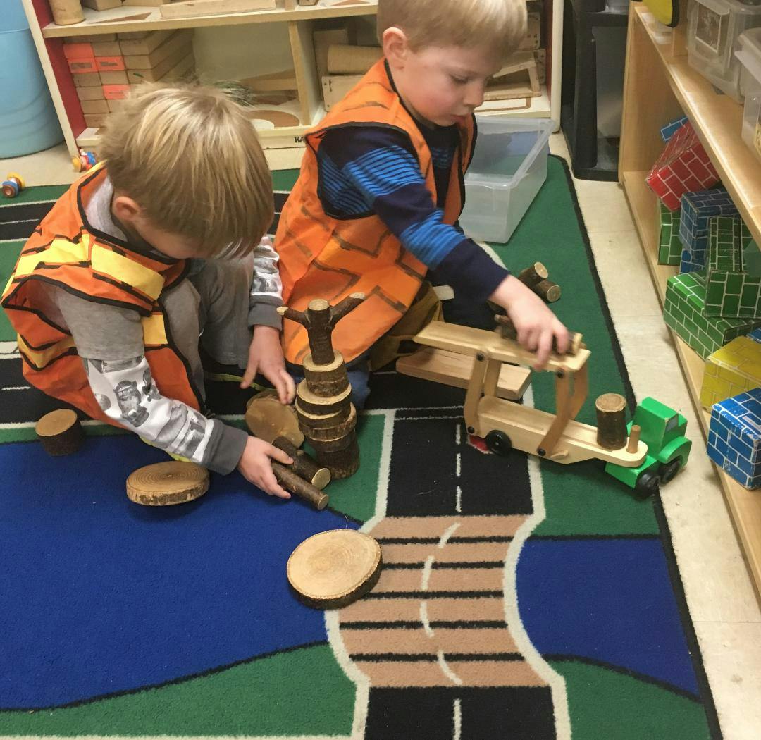 Two children playing with wooden blocks and toy trucks on a rug