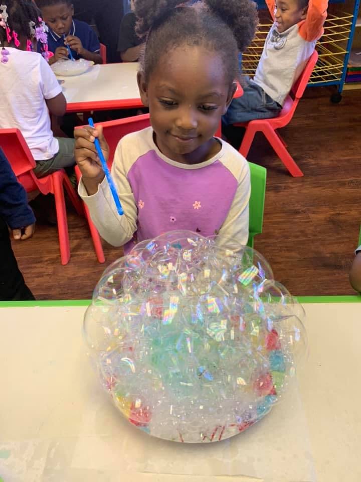 Child holding a blue stick over a pile of bubbles