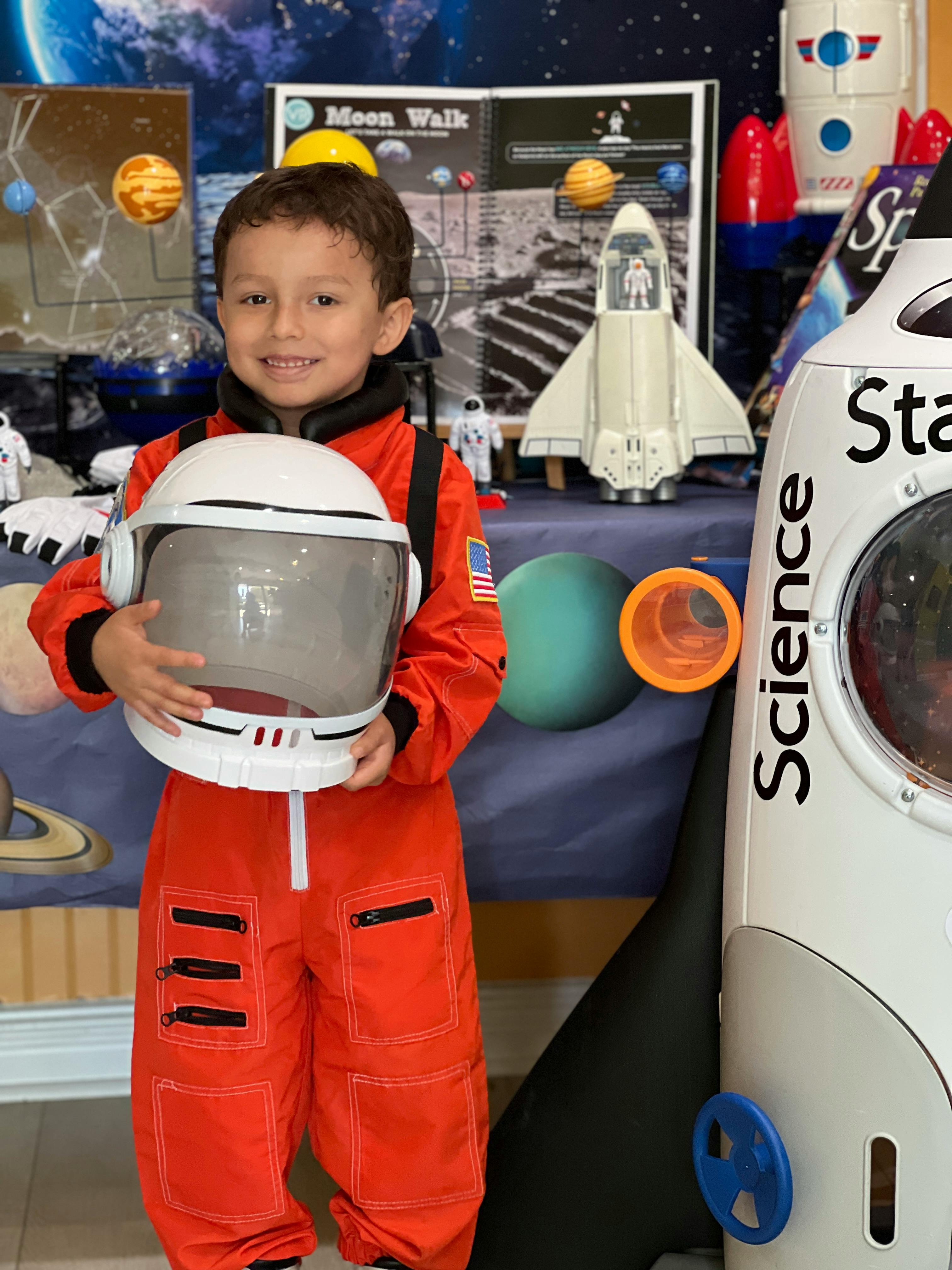 Child in orange astronaut suit holding a helmet