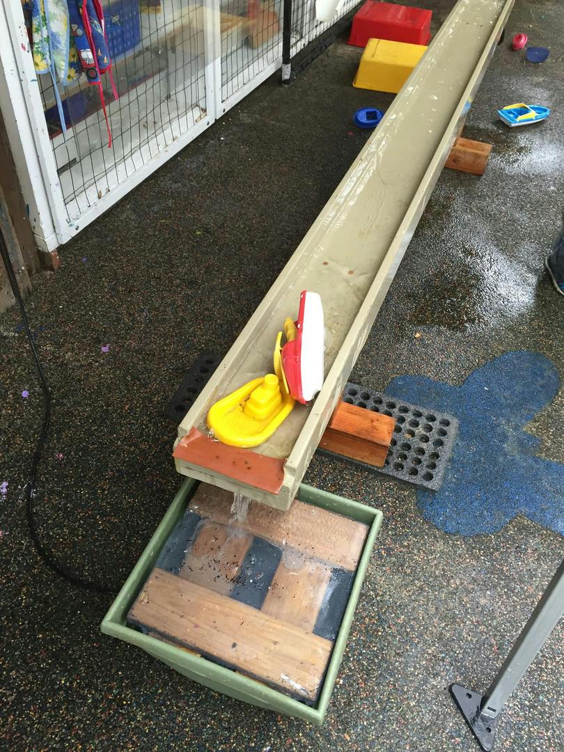 Toy boats in a water trough with water flowing into a basin