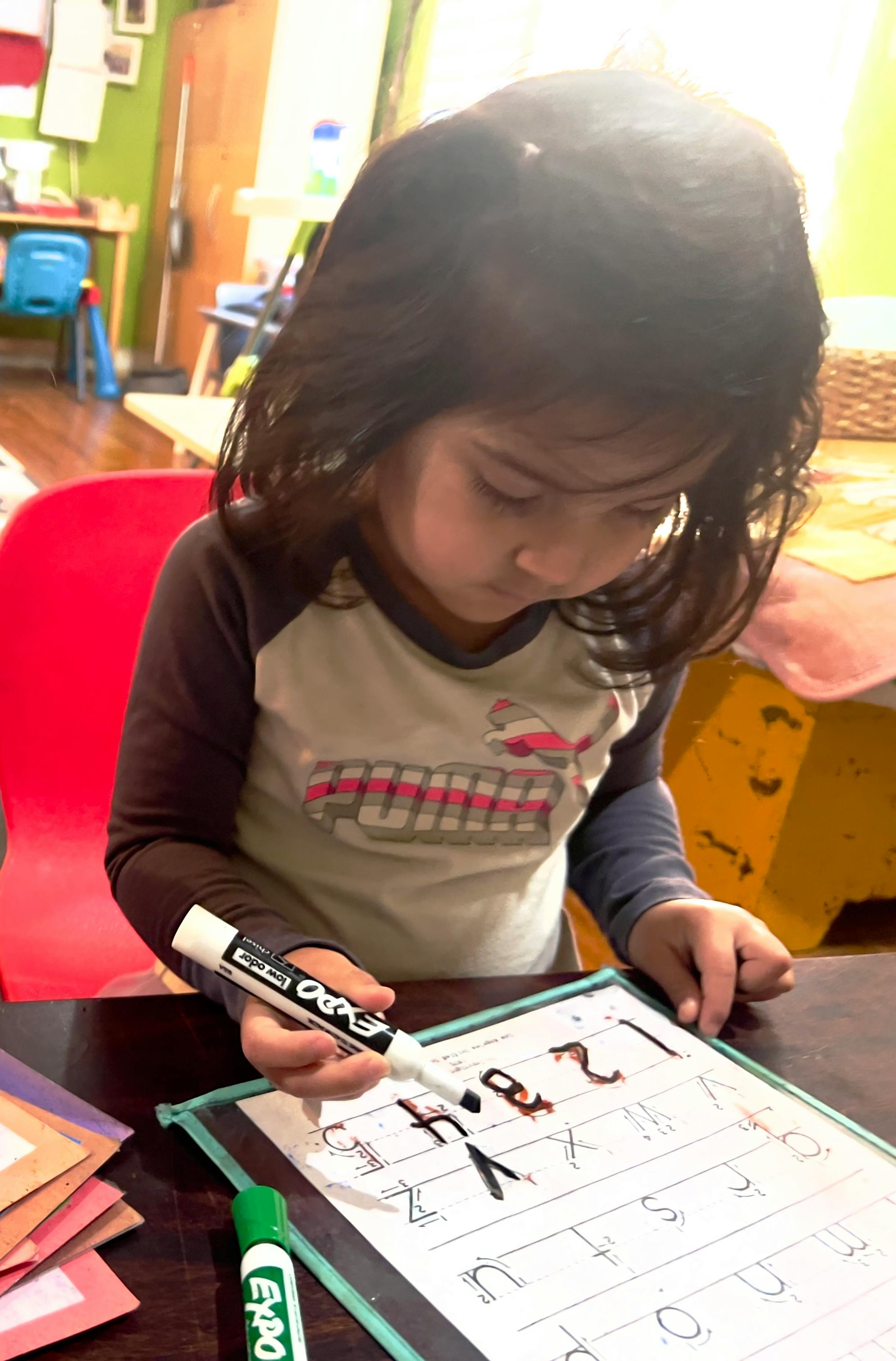 Child writing letters and numbers on a whiteboard with a marker