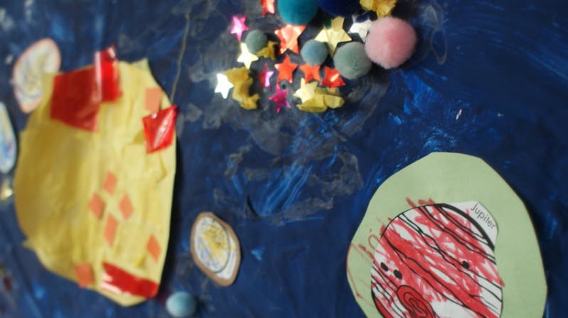 Child's artwork with paper cutouts and glitter on a blue background