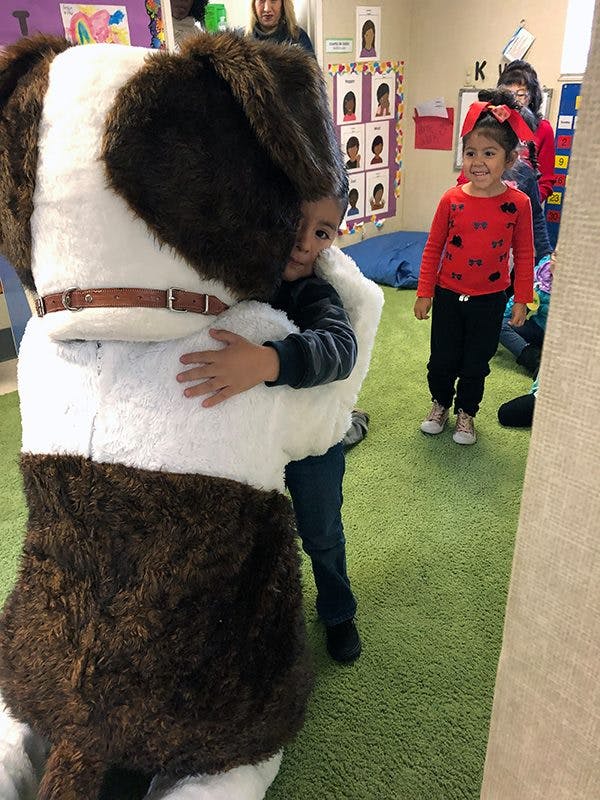 Child hugging a person in a large dog costume