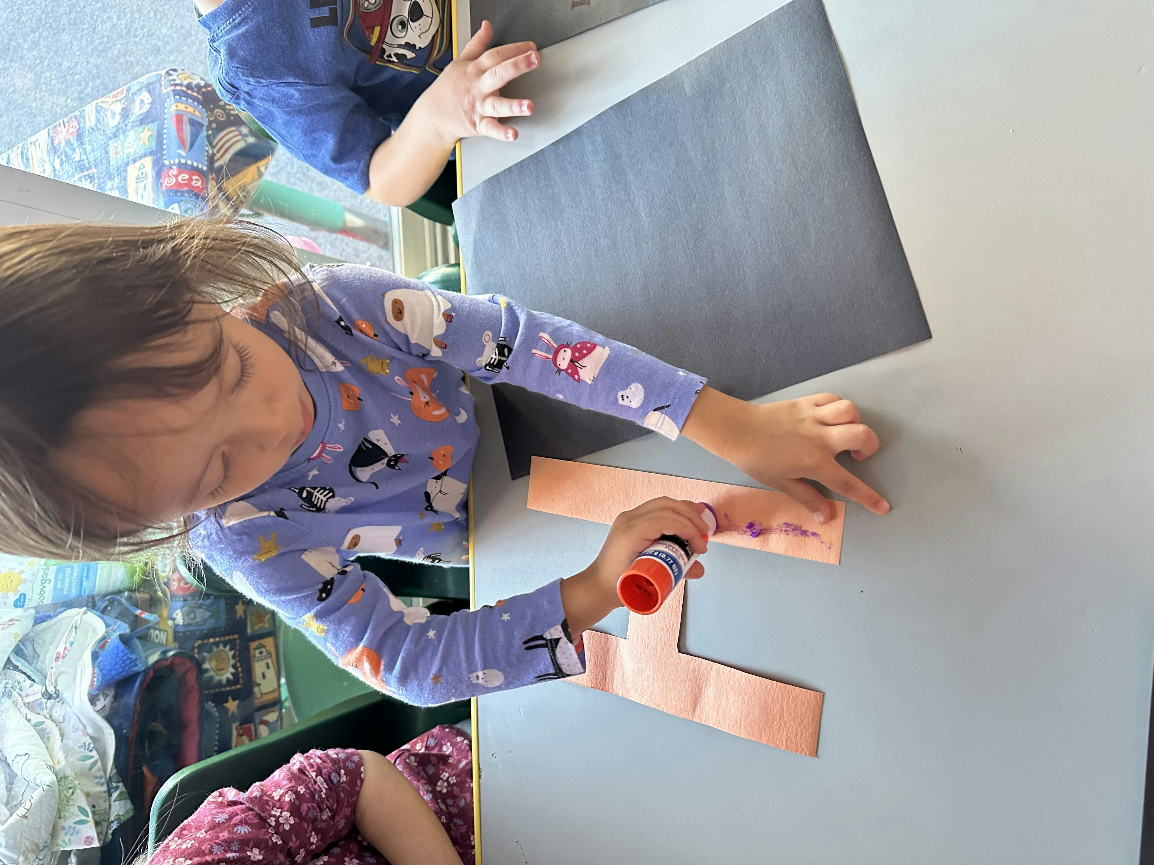 Child using a glue stick on paper shapes at a table