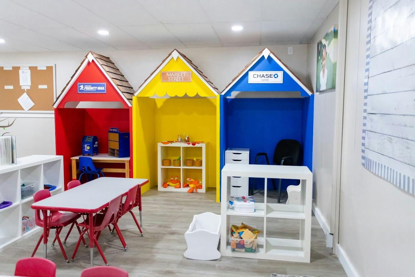 Play area with colorful house-shaped booths labeled post office market and bank