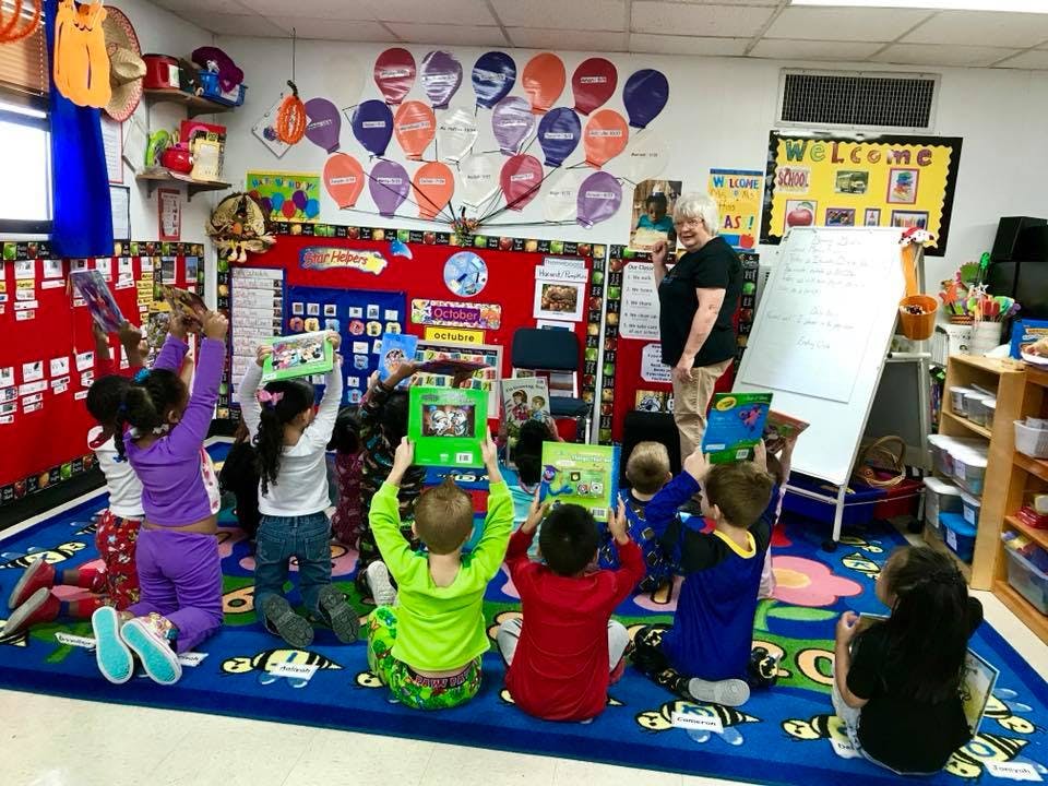 Children sitting on a rug holding books up in a classroom with an adult