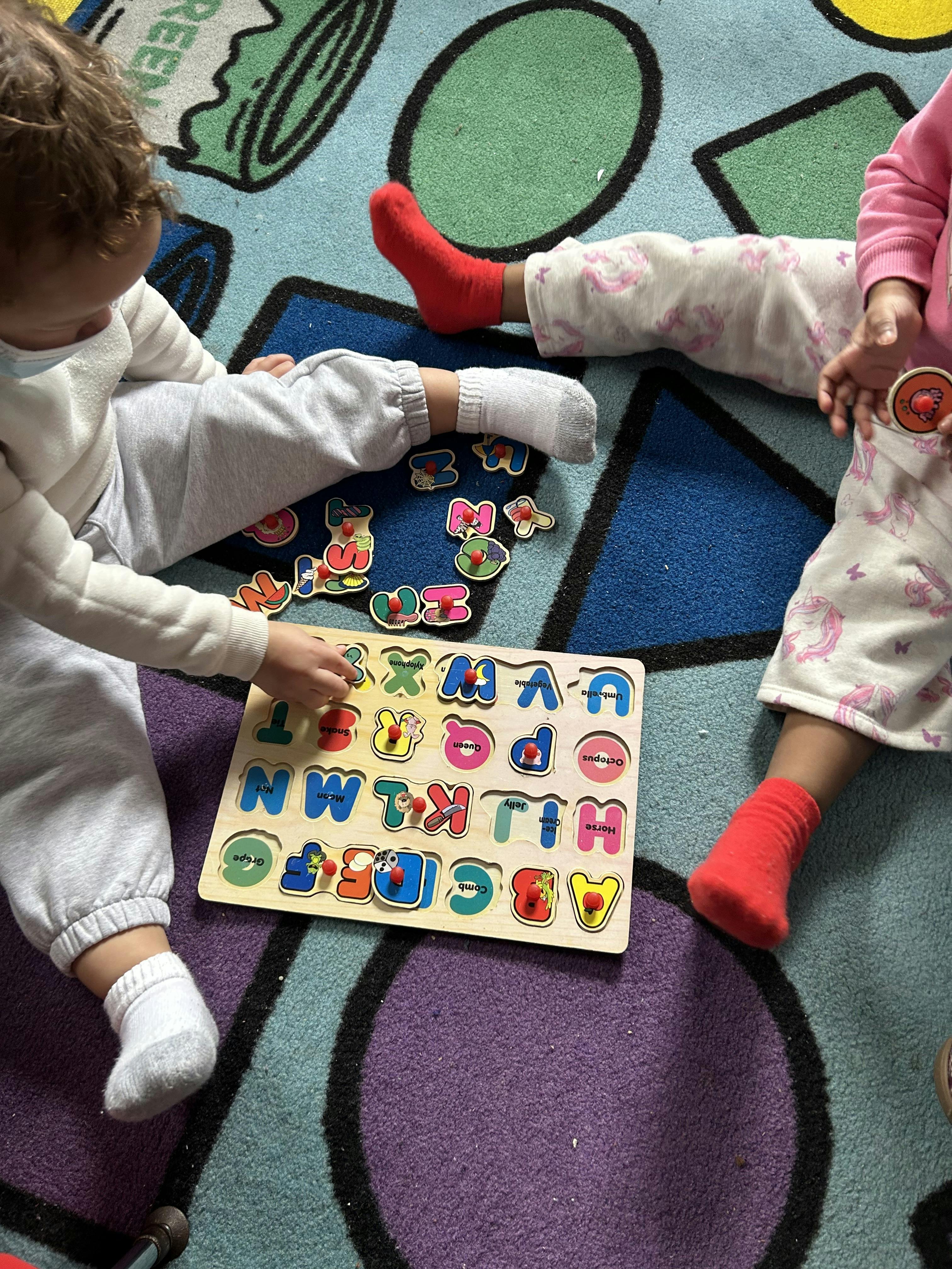 Two children playing with an alphabet puzzle on a colorful rug