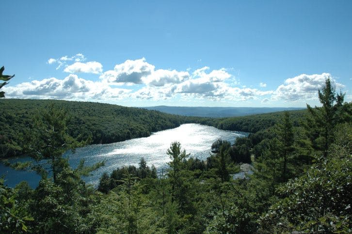 Aerial view of a lake surrounded by forested hills under a partly cloudy sky