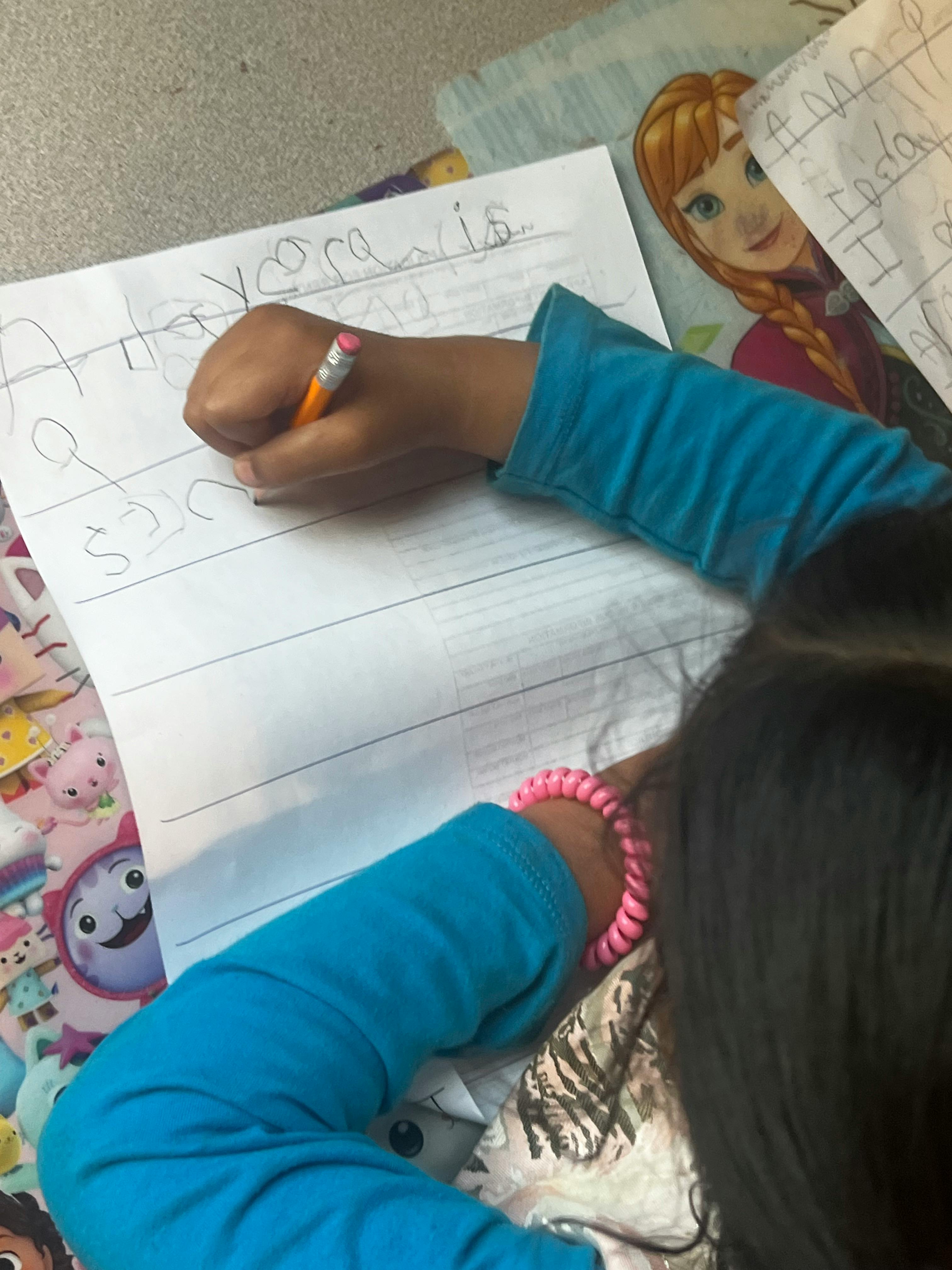 Child writing on lined paper with a pencil