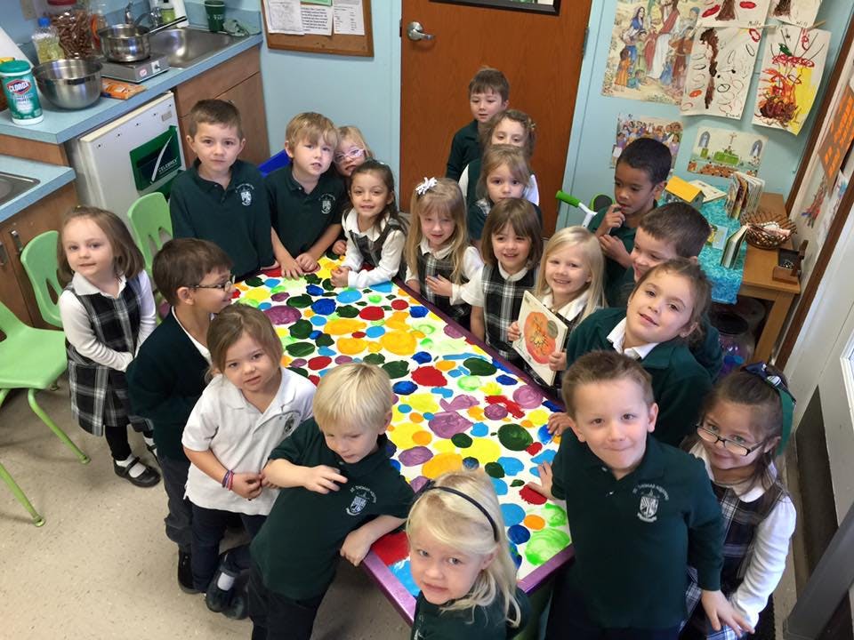 Group of children standing around a colorful table in a classroom