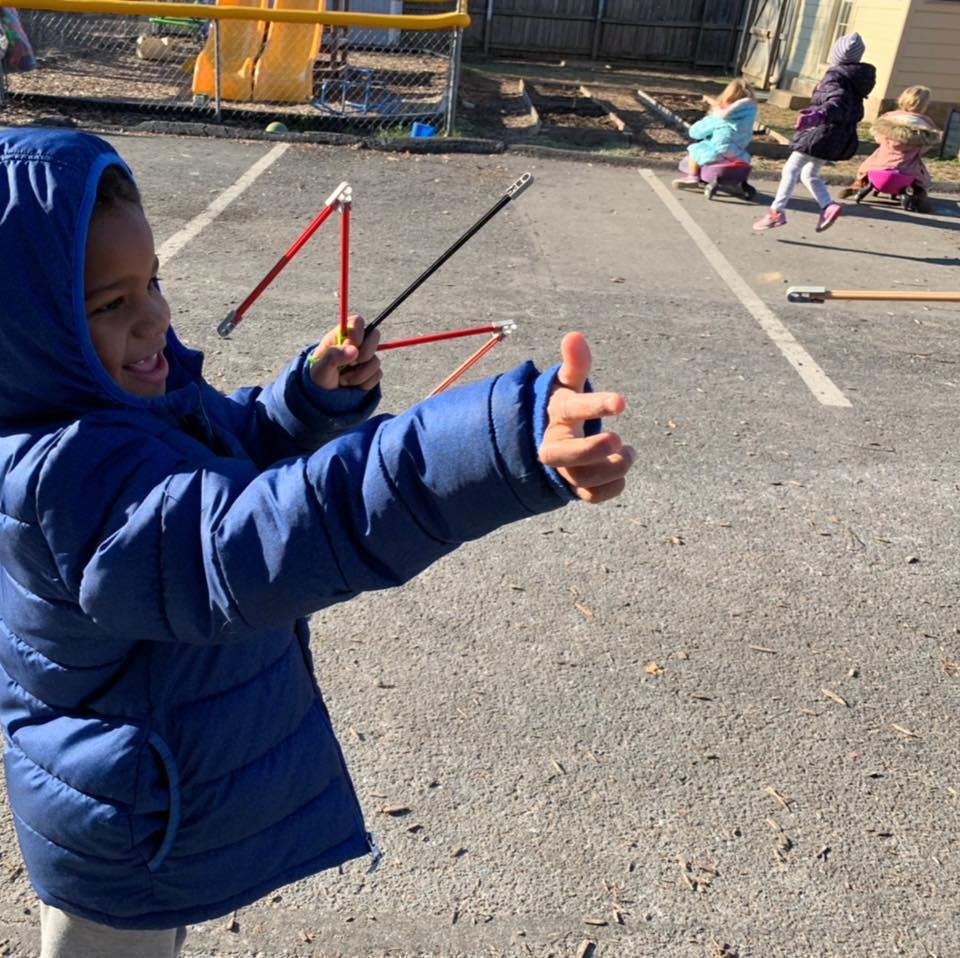 Child in blue coat holding sticks, aiming with hand