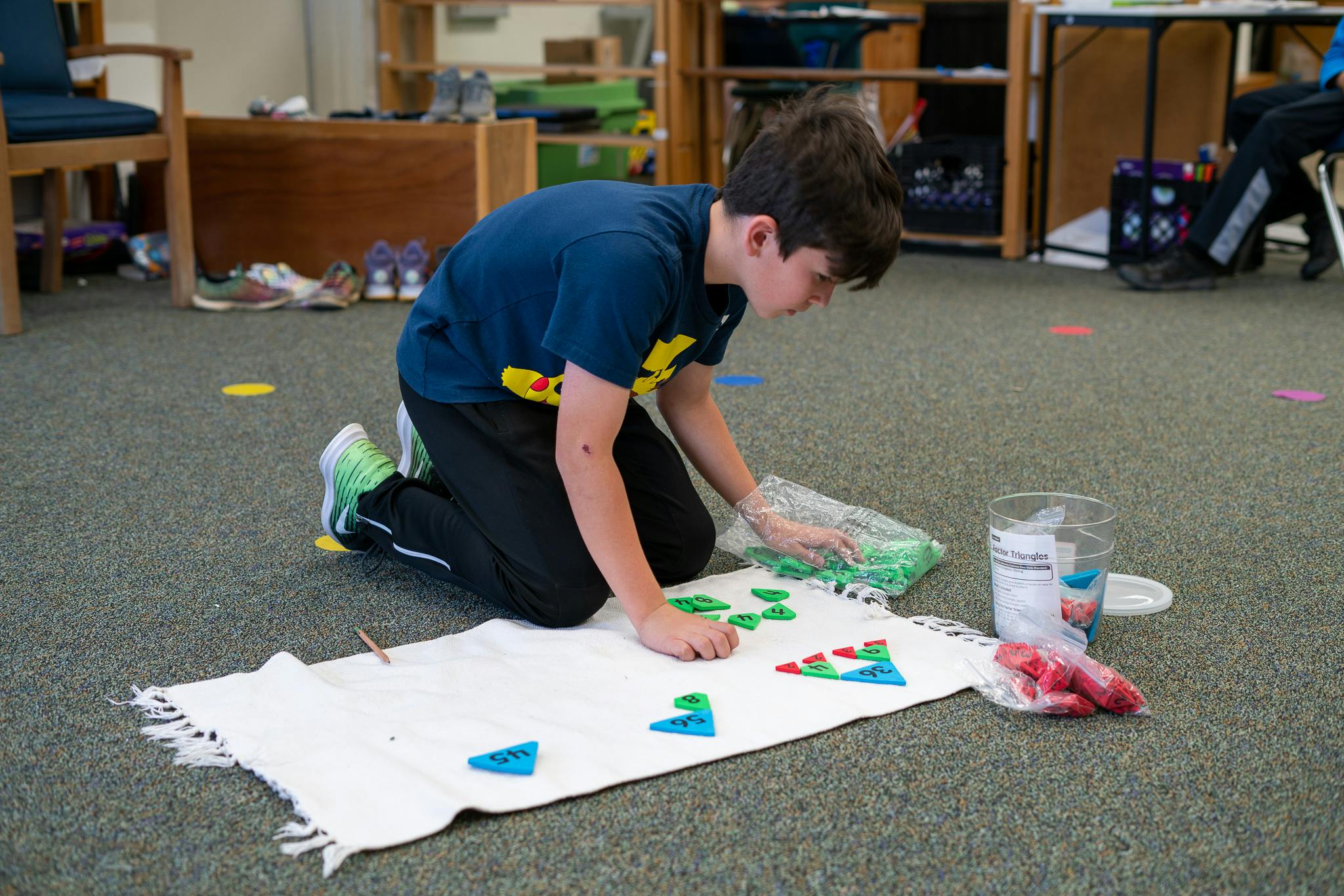 Child kneeling on floor arranging colorful shapes on a white mat