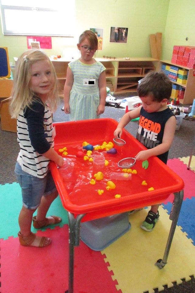 Three children playing with a water table filled with rubber ducks