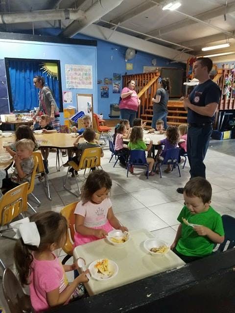 Children and adults in a large room, some children eating at tables