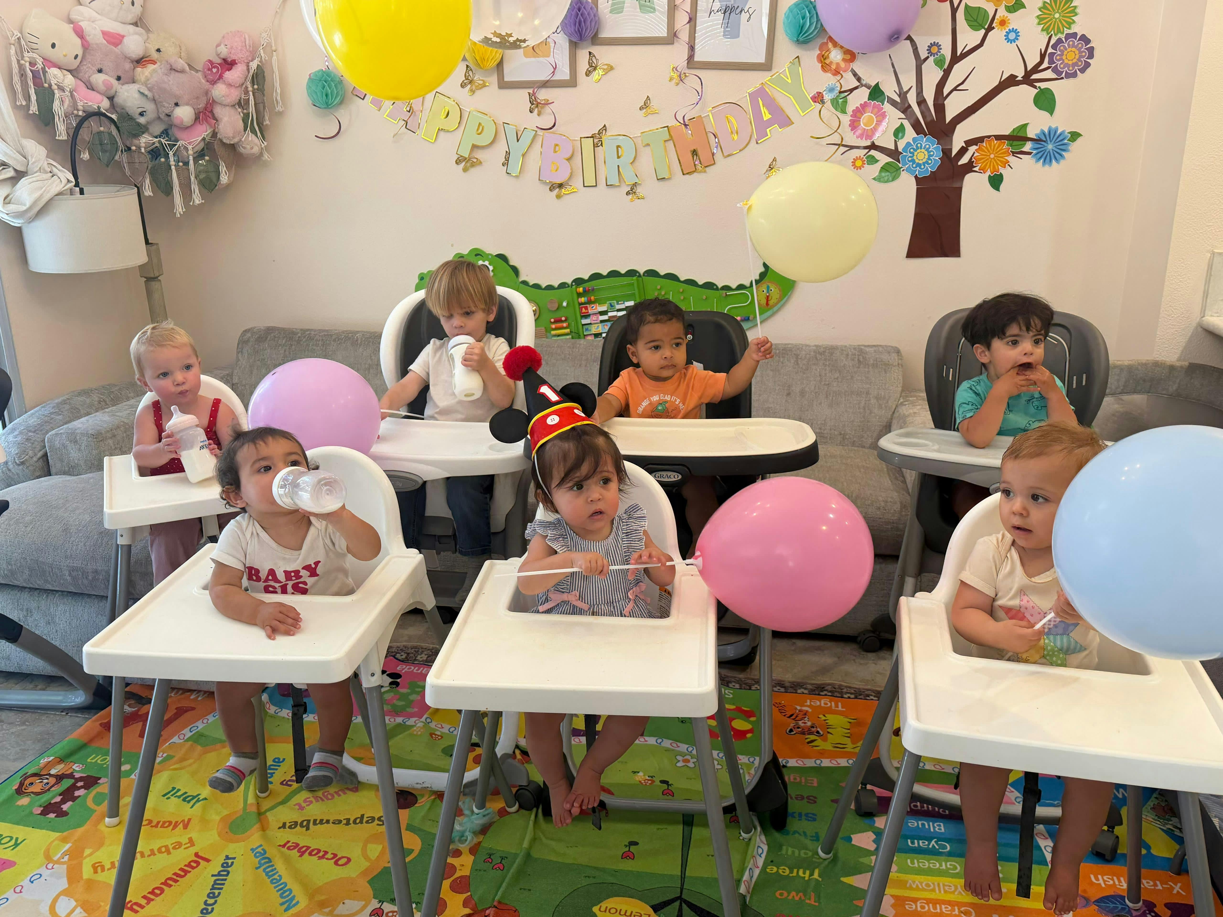 Group of children in high chairs celebrating a first birthday with balloons