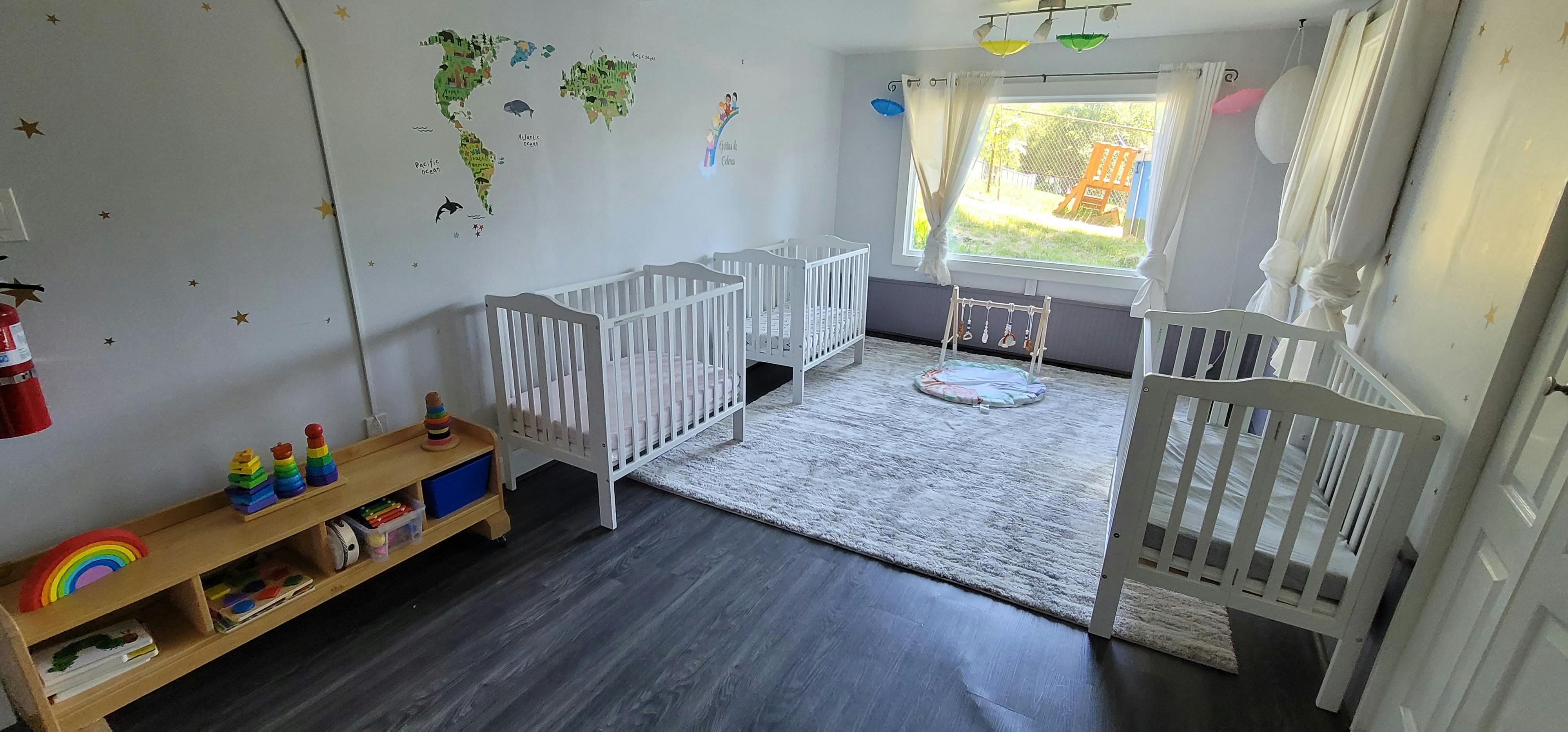 Three white cribs in a room with a rug and toys
