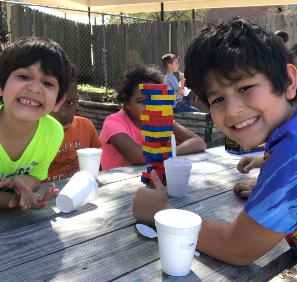 Children playing a stacking block game at a picnic table