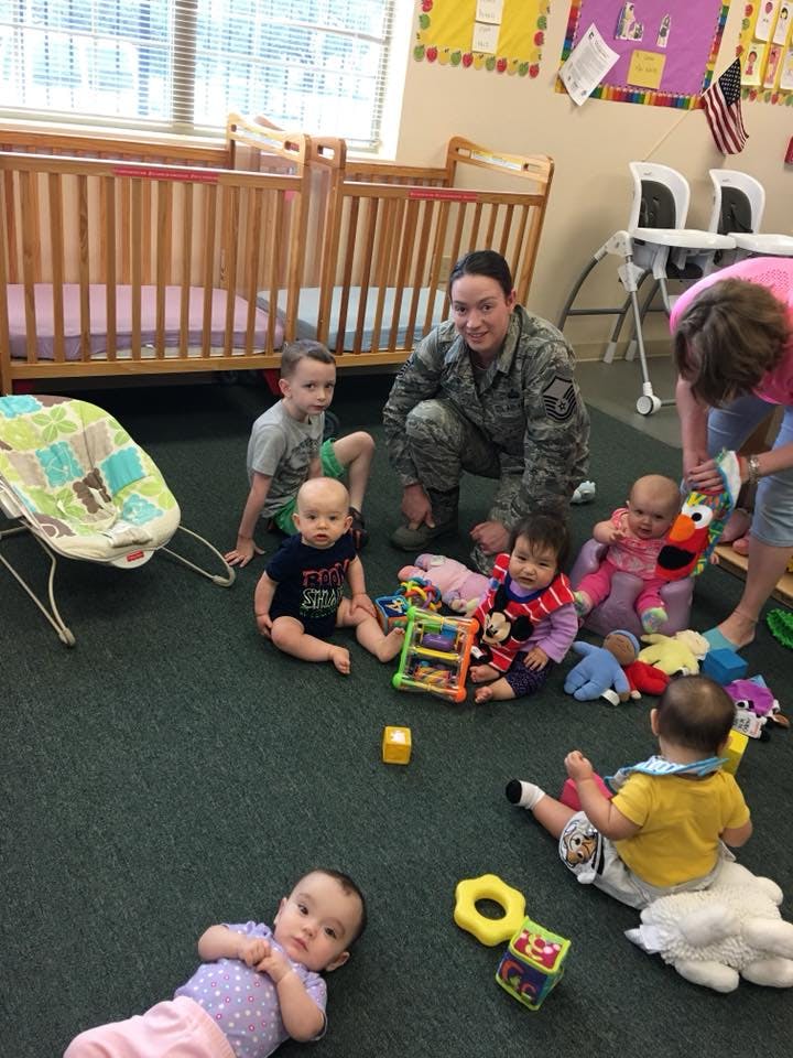 Adults and children on the floor with toys in a room with cribs