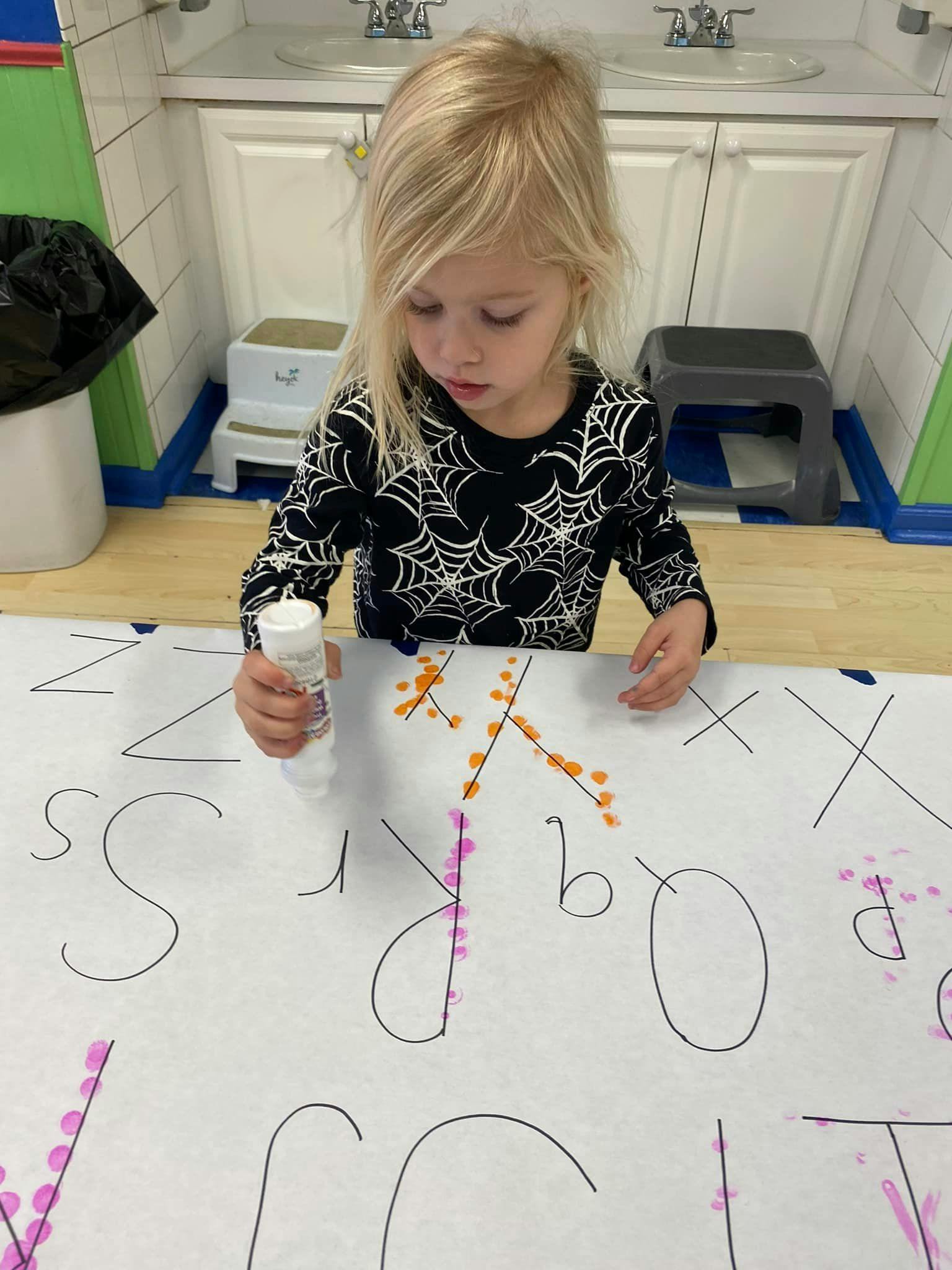 Child applying glue to a large sheet of paper with letters drawn letters