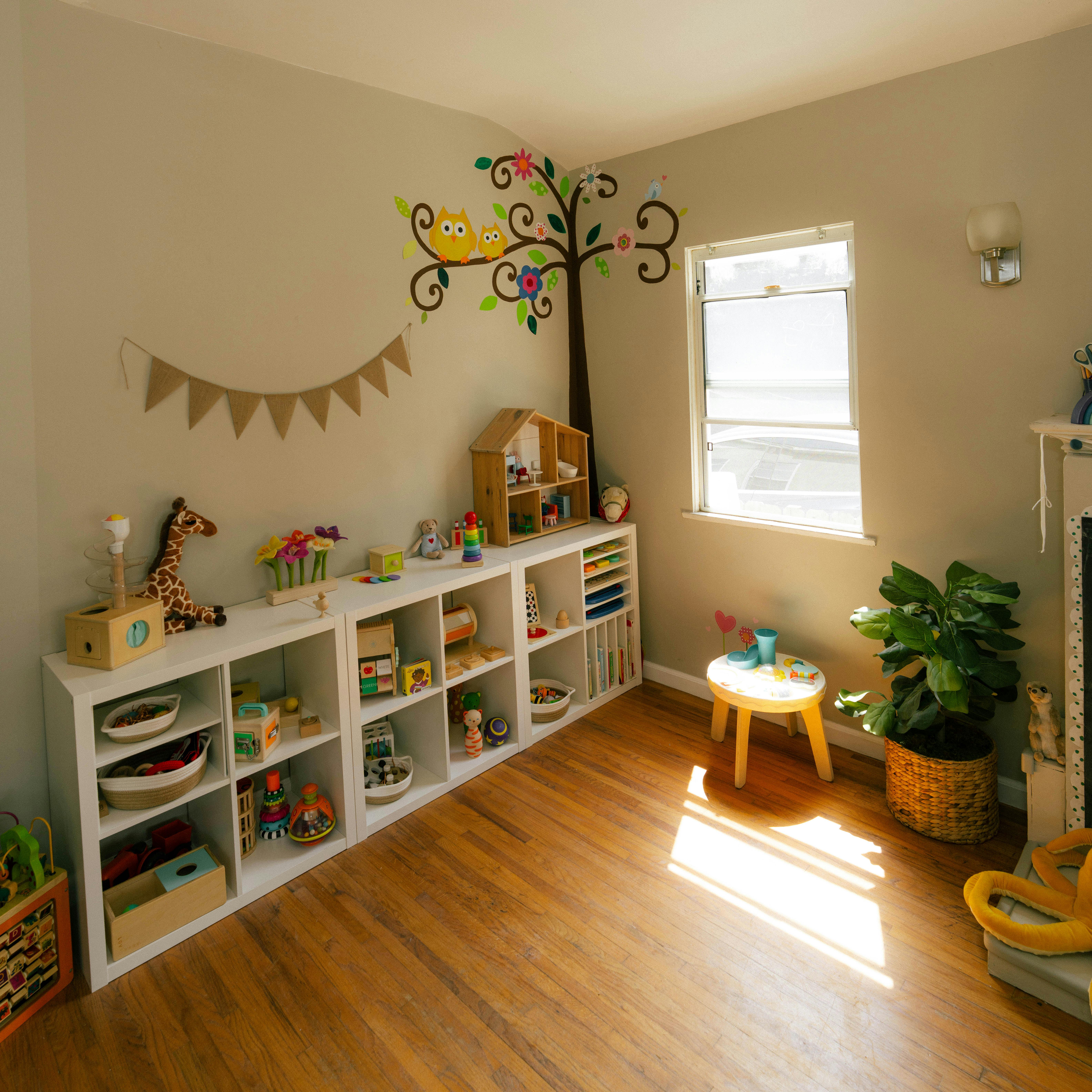 Playroom with white shelves filled with wooden toys and an owl wall decal