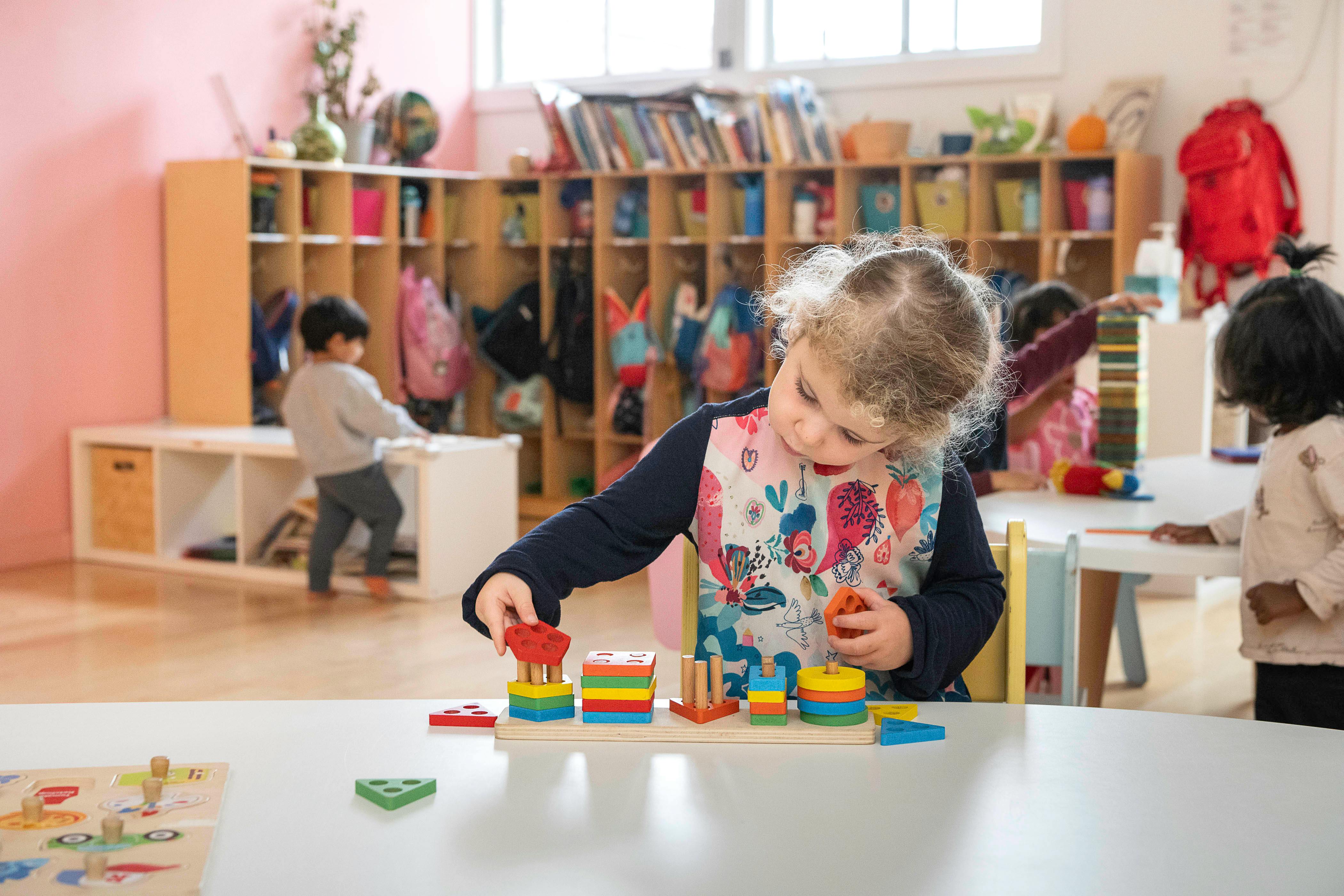 Child playing with a wooden stacking toy at a table in a classroom