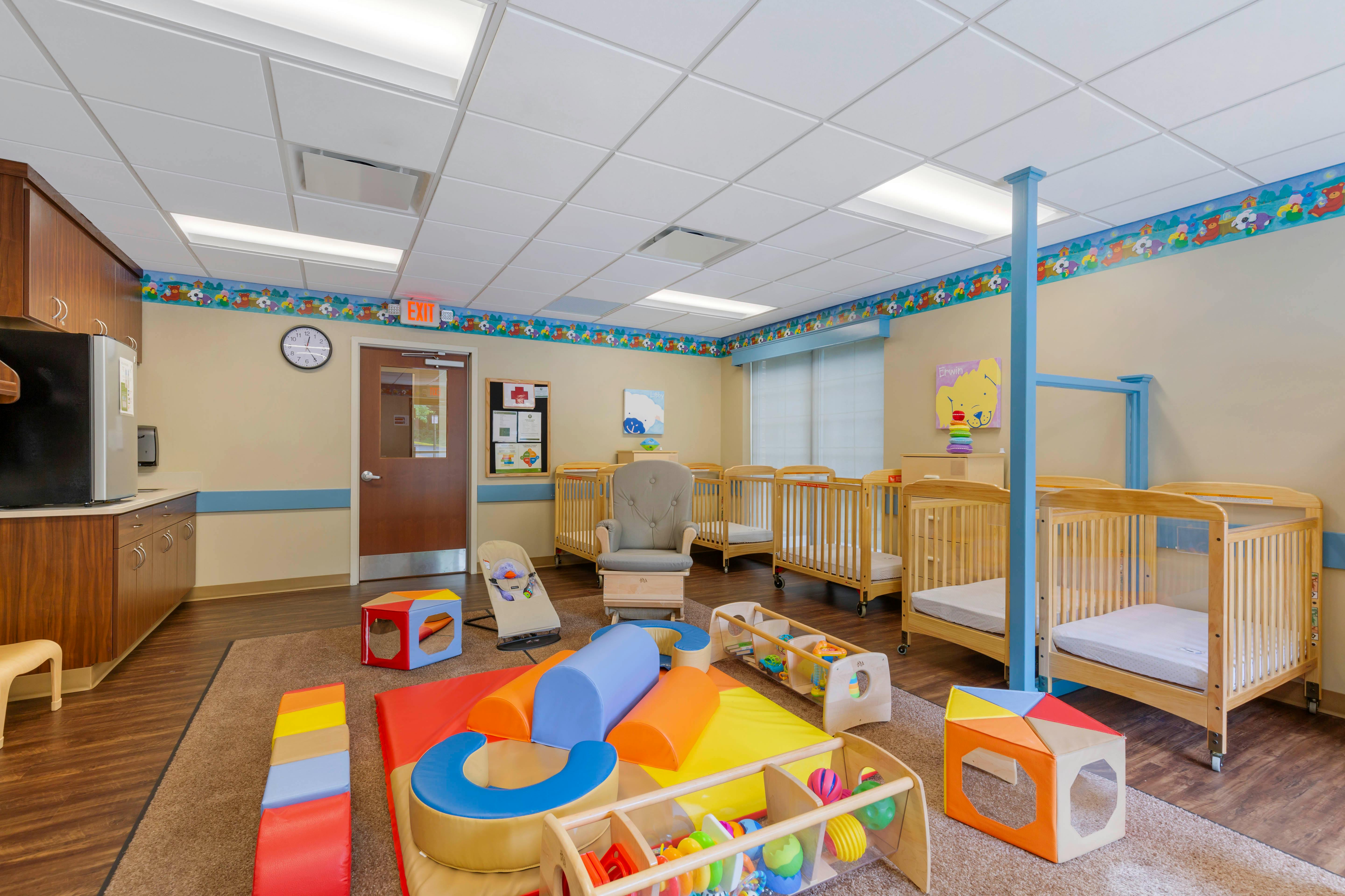 Childcare room with multiple cribs, a glider, and colorful play mats on the floor