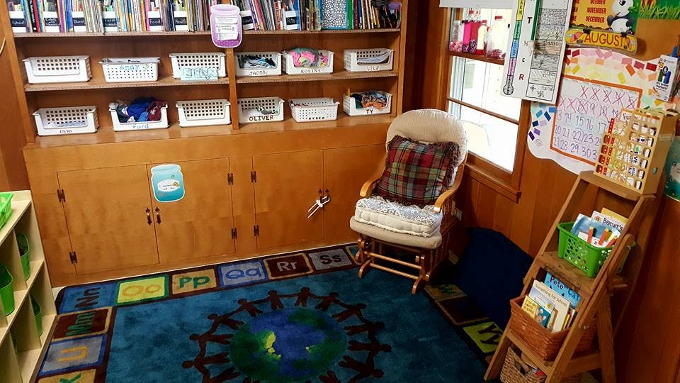 Classroom with bookshelves, a rocking chair, and a rug with letters