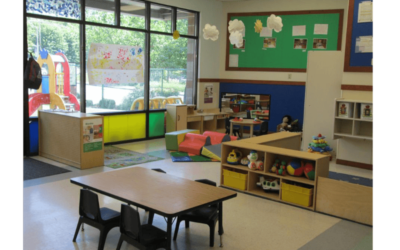 Empty classroom with small tables and chairs, toys, and large windows